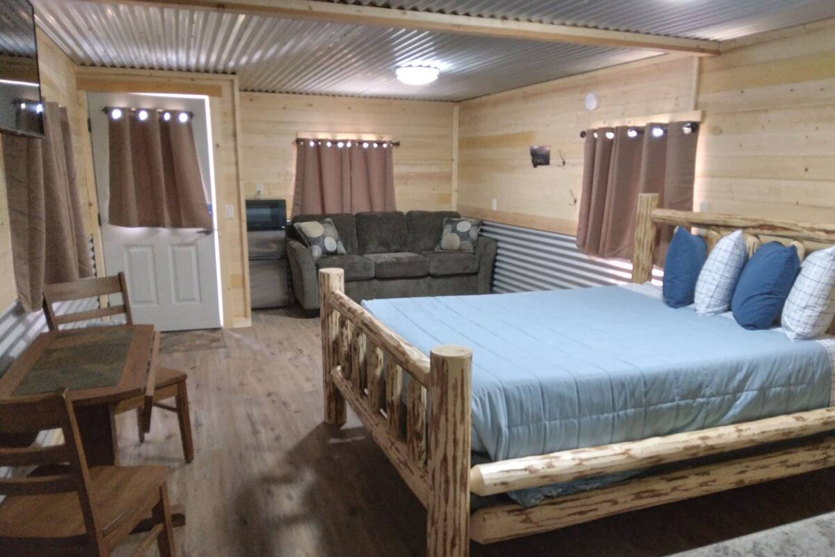 A wooden cabin room with a bed, a sofa, a table, and a chair.