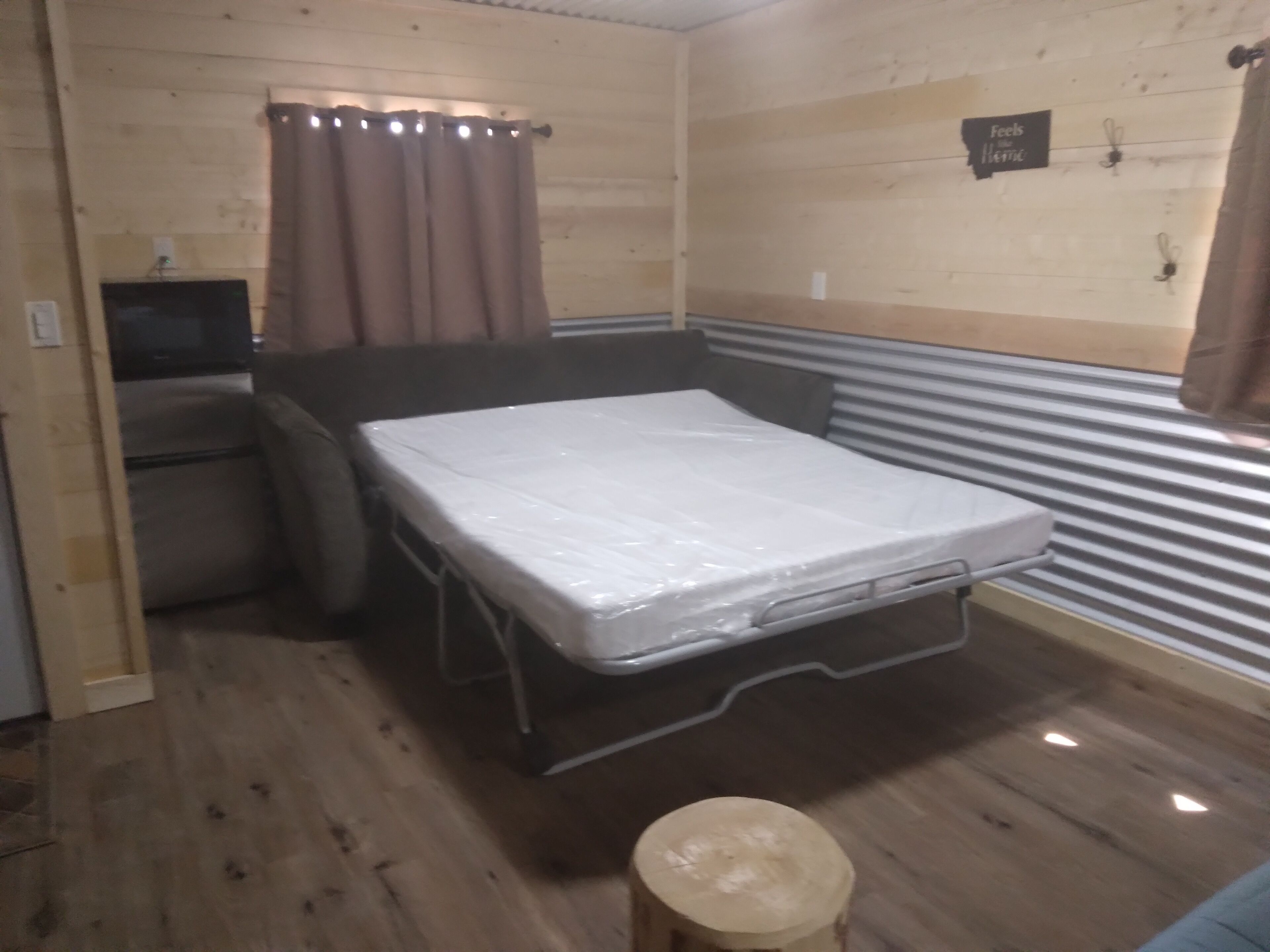 Habitación pequeña con cama, un taburete, televisor y un letrero en la pared.