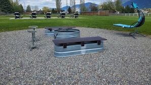 An outdoor seating area with metal tables and chairs, surrounded by gravel and greenery, with mountains in the background. - Glacier Acres Guest Ranch (Columbia Falls)