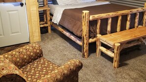 A wooden room with a bed, a bench, and a door. - Glacier Acres Guest Ranch (Columbia Falls)