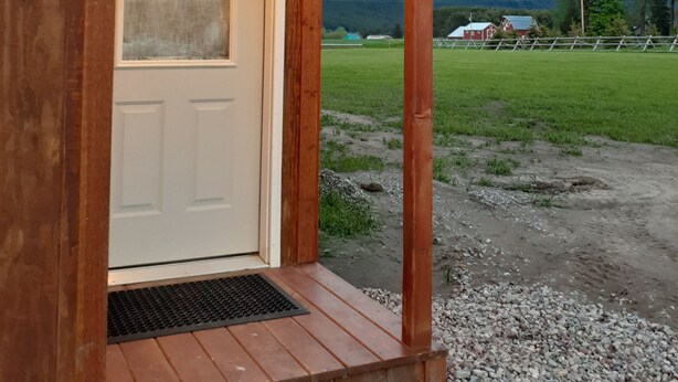 A wooden cabin with a white door and a small porch. - Glacier Acres Guest Ranch (Columbia Falls)