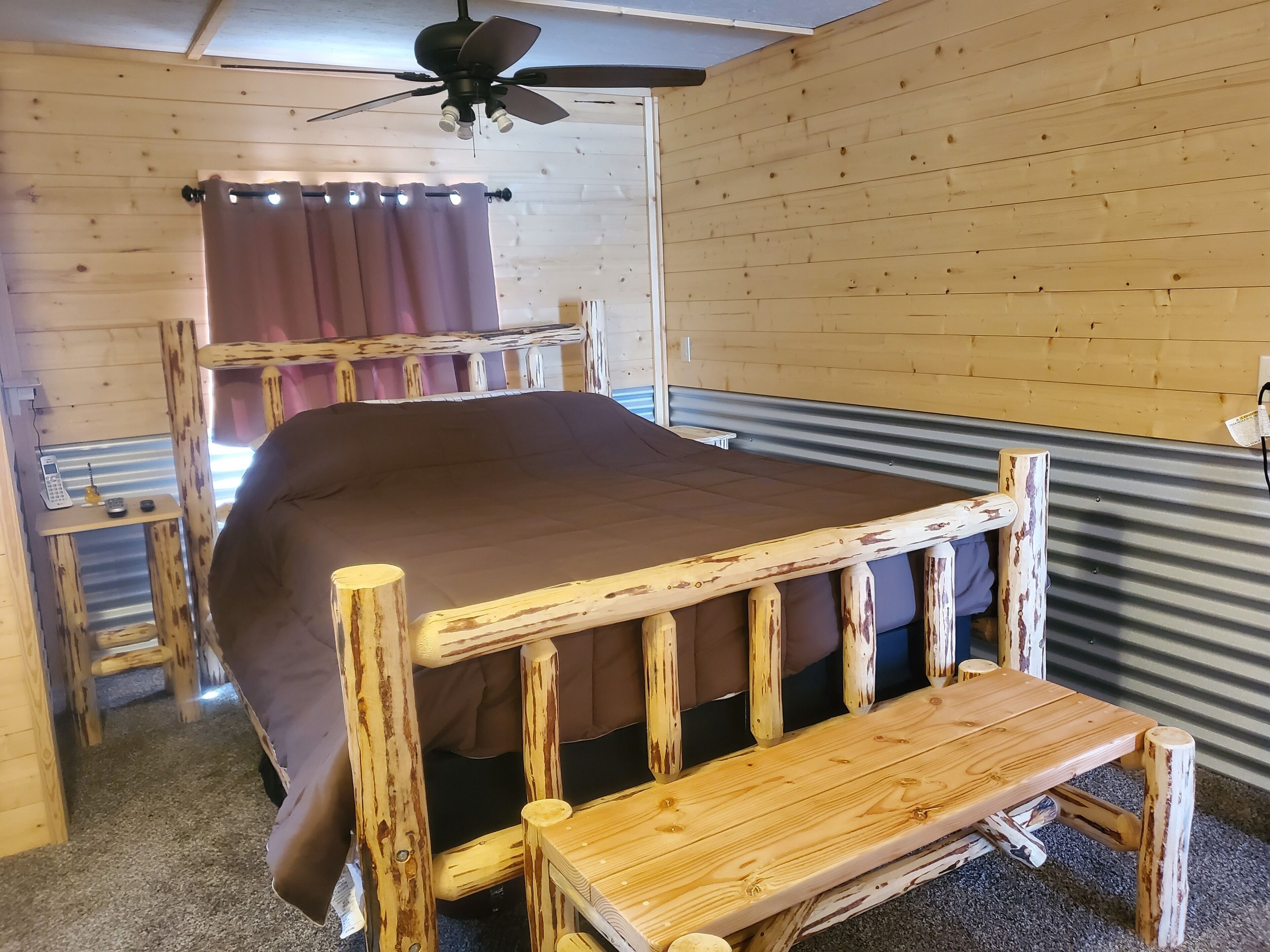 A wooden bunk bed with a bench, a ceiling fan, and a window with curtains.