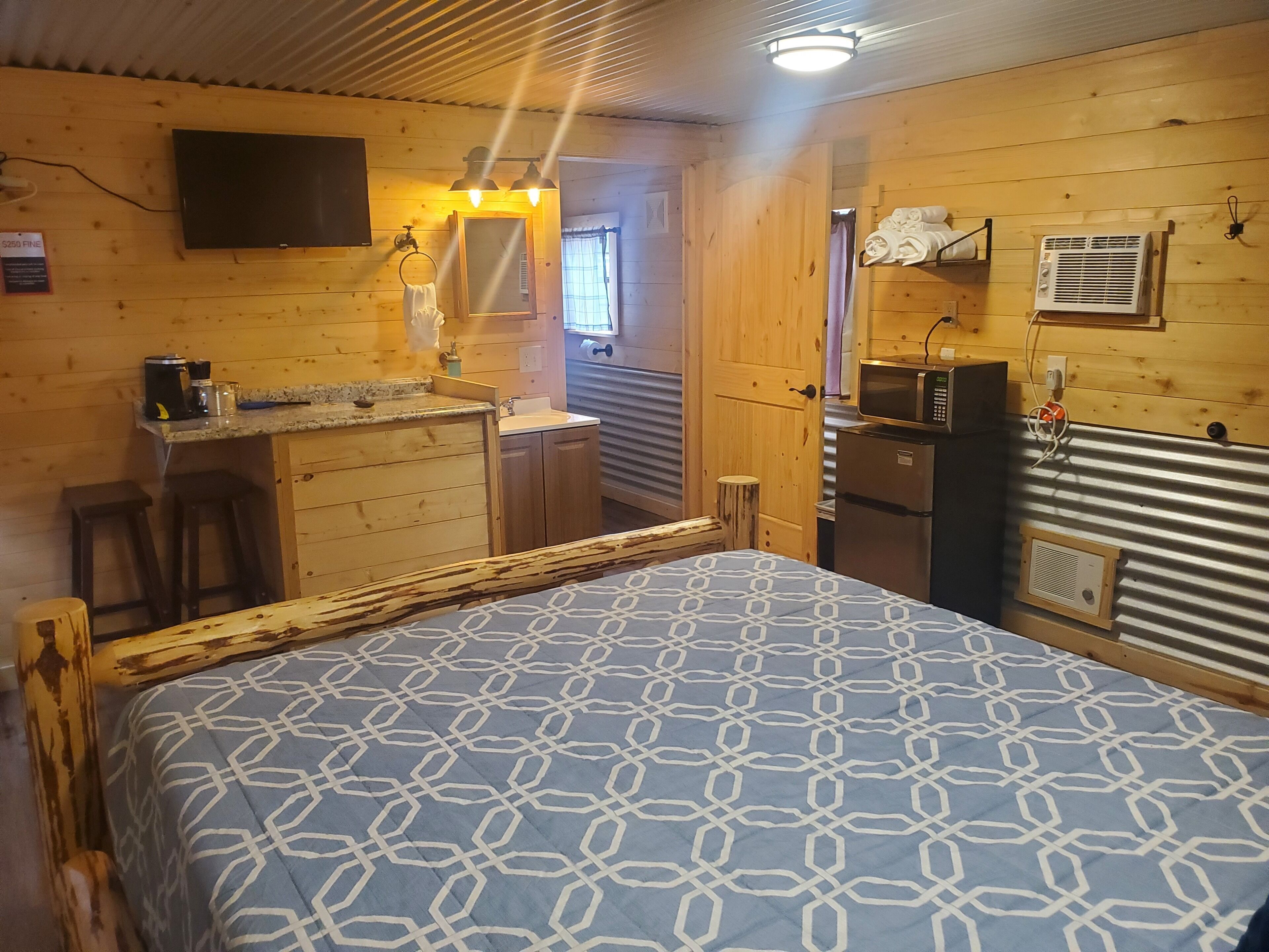 Une chambre confortable, aménagée dans le style d’un chalet, avec un lit, une petite kitchenette, une télévision et une salle de bain avec douche.
