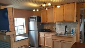A compact kitchen with wooden cabinets, a stainless steel refrigerator, a microwave, a sink, and a trash bin. - Glacier Acres Guest Ranch (Columbia Falls)