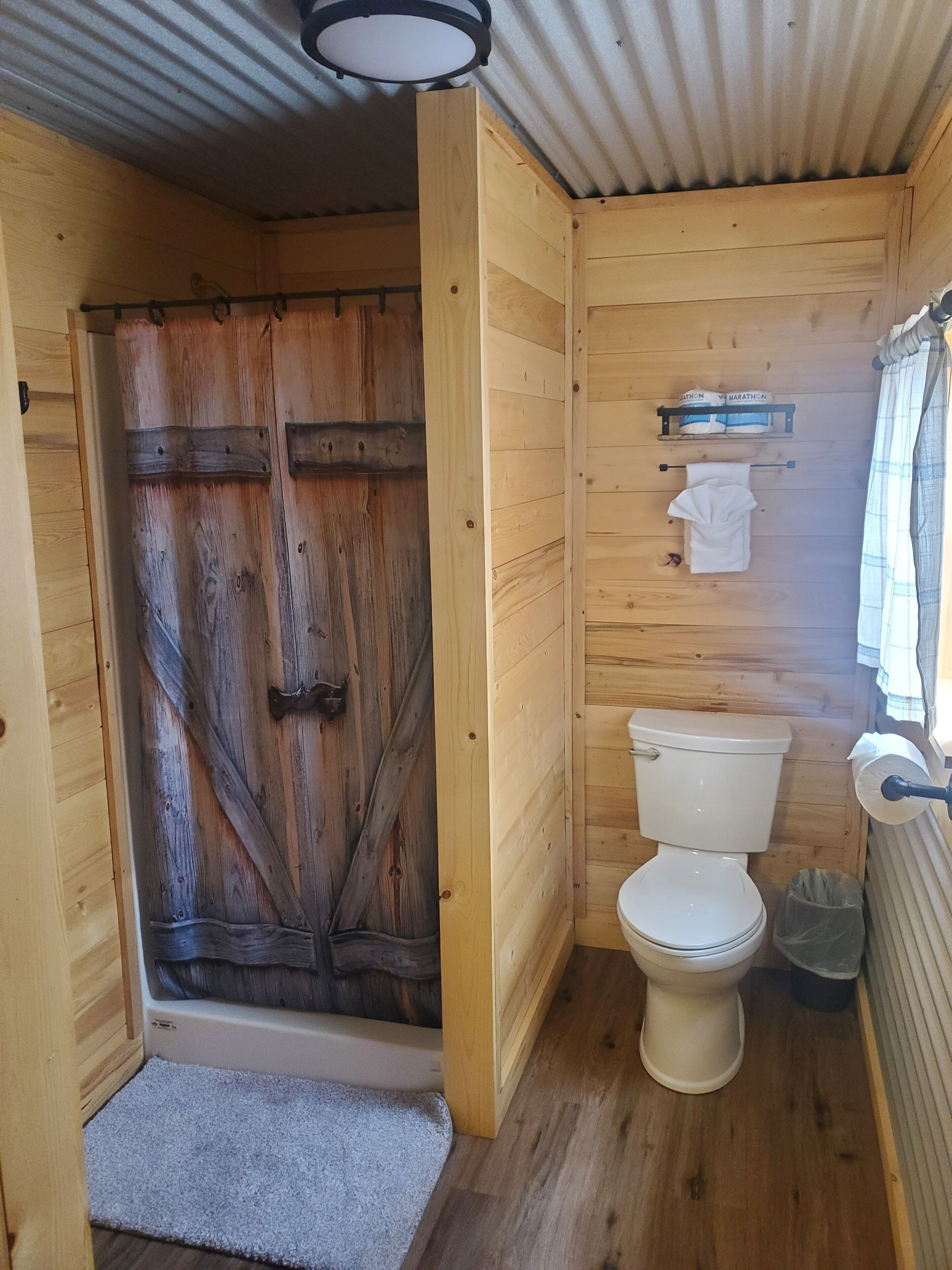 A wooden bathroom with a white toilet, a towel hanging on a rack, and a shower door.