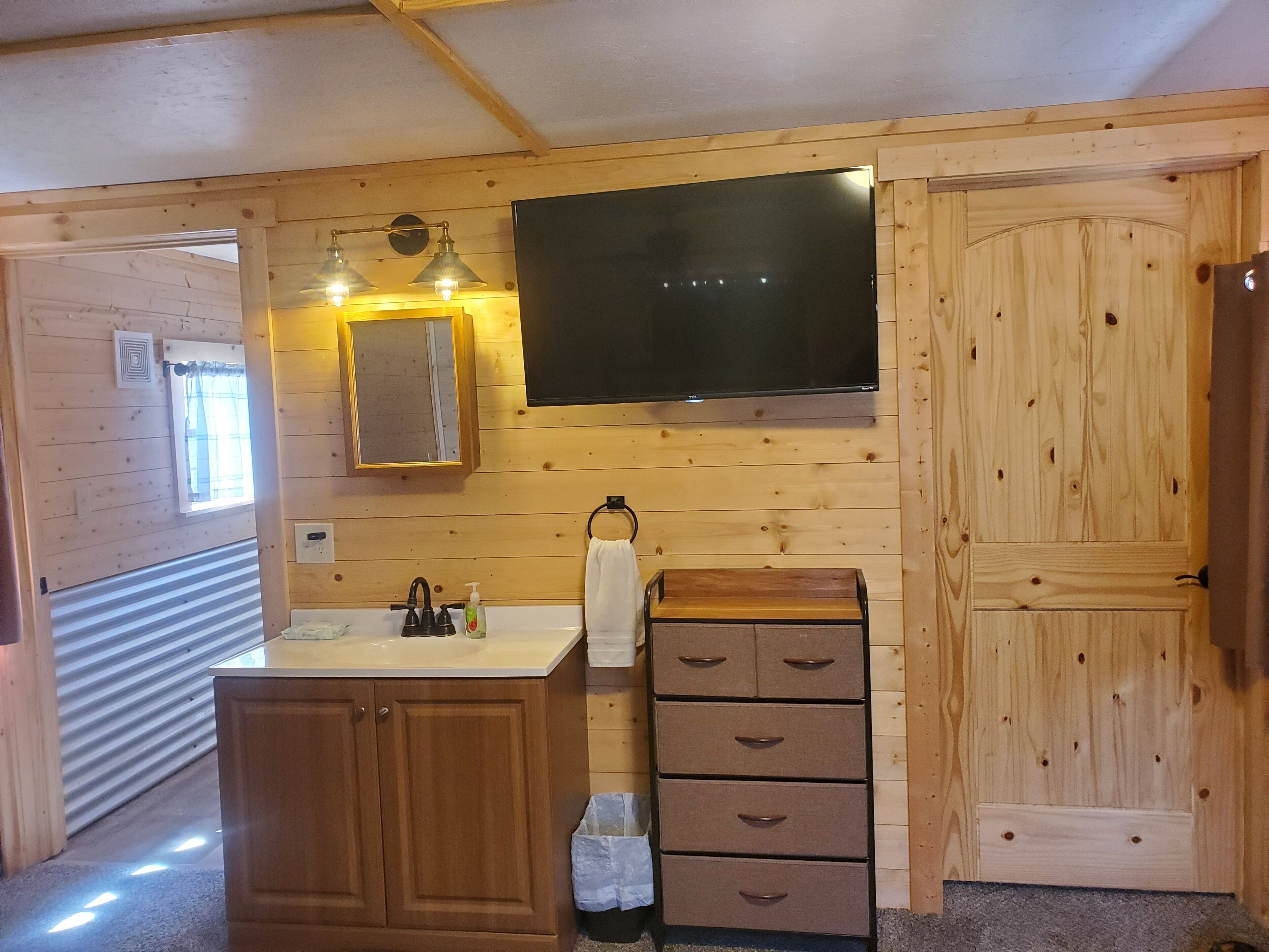 Une salle de bain rustique, aménagée dans une cabane en bois, avec un lavabo, un miroir et un téléviseur fixé au mur.