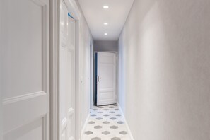 A hallway with white walls, a white door at the end, and a patterned floor.