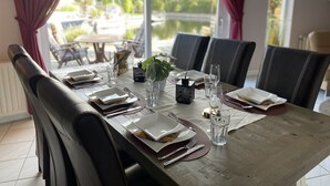 A dining table set with plates, cutlery, and glasses, with a view of the outdoors through large windows.