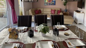 A dining area with a table set for four, two pendant lights, a painting on the wall, and a sofa in the background.