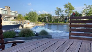 A wooden deck with a view of a canal, boats, and greenery.