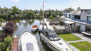 A marina with boats docked, a modern house with a deck, and a river in the background.