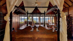 A wooden room with a canopy bed, a ceiling fan, and a view of the ocean. - Jasri Bay Hideaway (Karangasem)