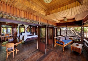 A wooden cabin with a bed, a sofa, and a dining table. - Jasri Bay Hideaway (Karangasem)
