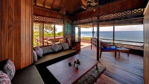A wooden interior with a large window overlooking the ocean, a seating area with cushions, and a small table with decorative items. - Jasri Bay Hideaway (Karangasem)