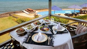 A dining table set with various dishes, overlooking a pool and the ocean. - Jasri Bay Hideaway (Karangasem)