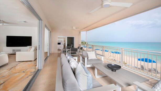 Een ruim balkon met uitzicht op het strand, een flatscreen televisie en een eethoek met terrasmeubels.