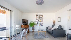 A modern living room with a glass dining table, grey sofa, and a large wall art piece. - Appartement Panorama - Welkeys (Villeneuve-Loubet)