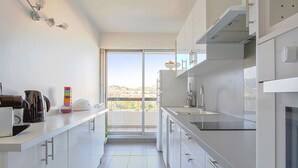 A modern kitchen with white cabinetry, a large window, and a view of the outdoors. - Appartement Panorama - Welkeys (Villeneuve-Loubet)