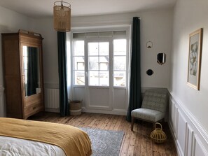 Quarto com guarda-roupa de madeira, cama com manta amarela, cadeira, janela com cortinas e luminária pendente.