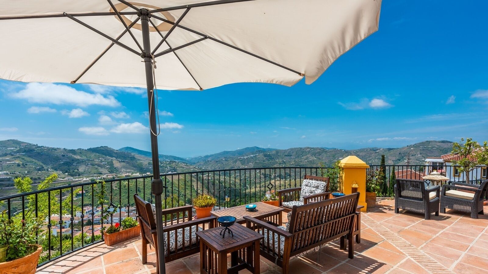 Une terrasse avec une table et des chaises, un grand parasol et une vue sur les montagnes.
