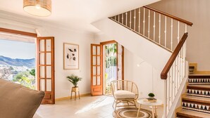 A spacious living area with a view of the city, a wooden staircase, and a wicker chair.
