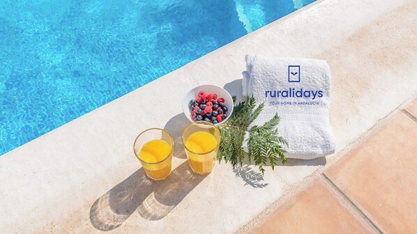 A poolside setting with a towel, a bowl of berries, and two glasses of orange juice.