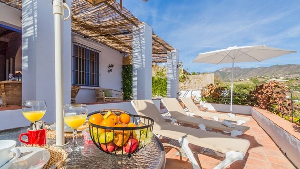 A terrace with a fruit bowl, lounge chairs, and a table with drinks and a red mug.