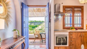 A kitchen with a view of a green landscape, a dining area with a table and chairs, and a blue door leading to an outdoor area.