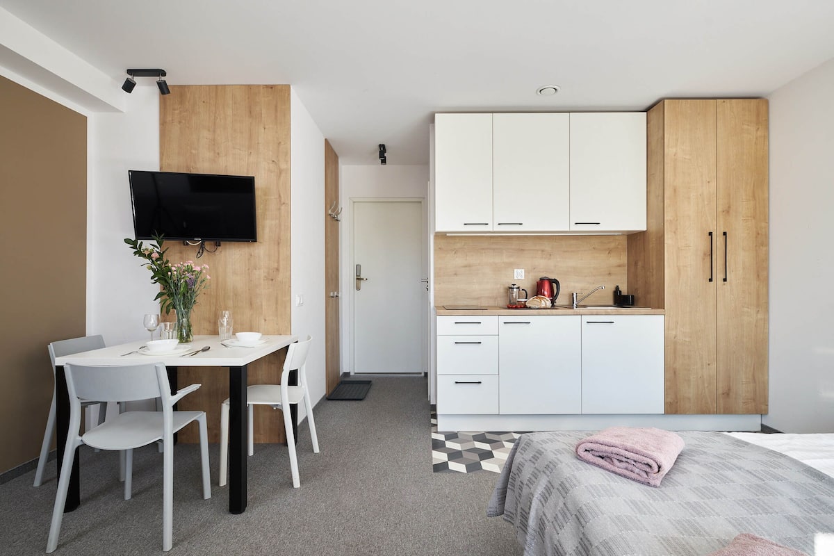 Una habitación de hotel moderna con zona de comedor, cama y una kitchenette con toalla rosa.