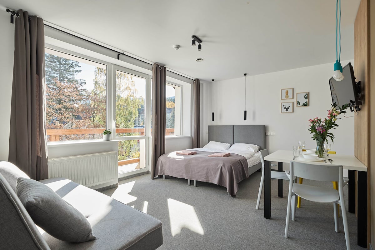 Un dormitorio moderno con cama, sofá, mesa de comedor con sillas y televisor montado en la pared.