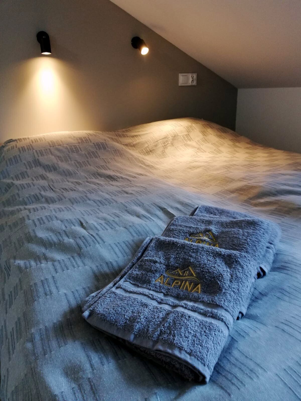 Una cama con una toalla doblada, una lámpara de pared y un termostato.