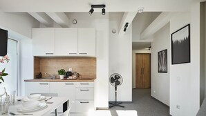 A modern kitchen with white cabinets, a wooden countertop, and a dining area with a table set for two. - Villa Alpina (Szklarska Poreba)