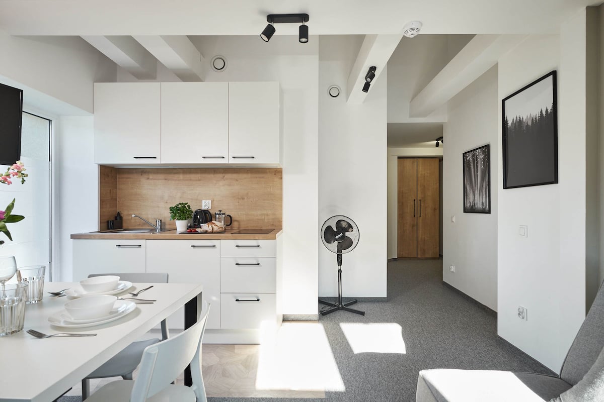 Una cocina moderna con armarios blancos, encimera de madera y un comedor con una mesa para dos.