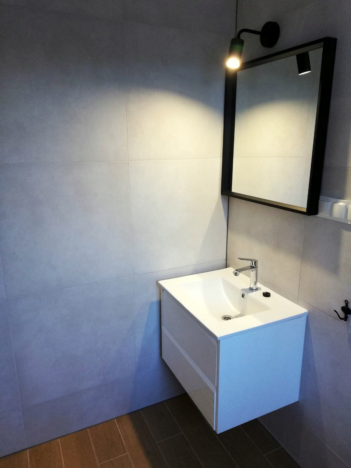 A modern bathroom with a white sink, a mirror, and a wall-mounted light fixture.