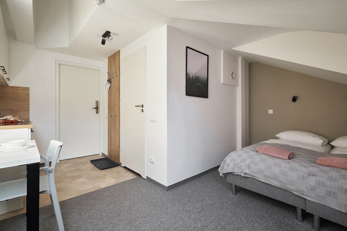 Un dormitorio con cama, escritorio y silla. Hay una puerta que da a otra habitación.