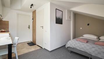 Ein Schlafzimmer mit Bett, Schreibtisch und Stuhl. Eine Tür führt in einen anderen Raum.