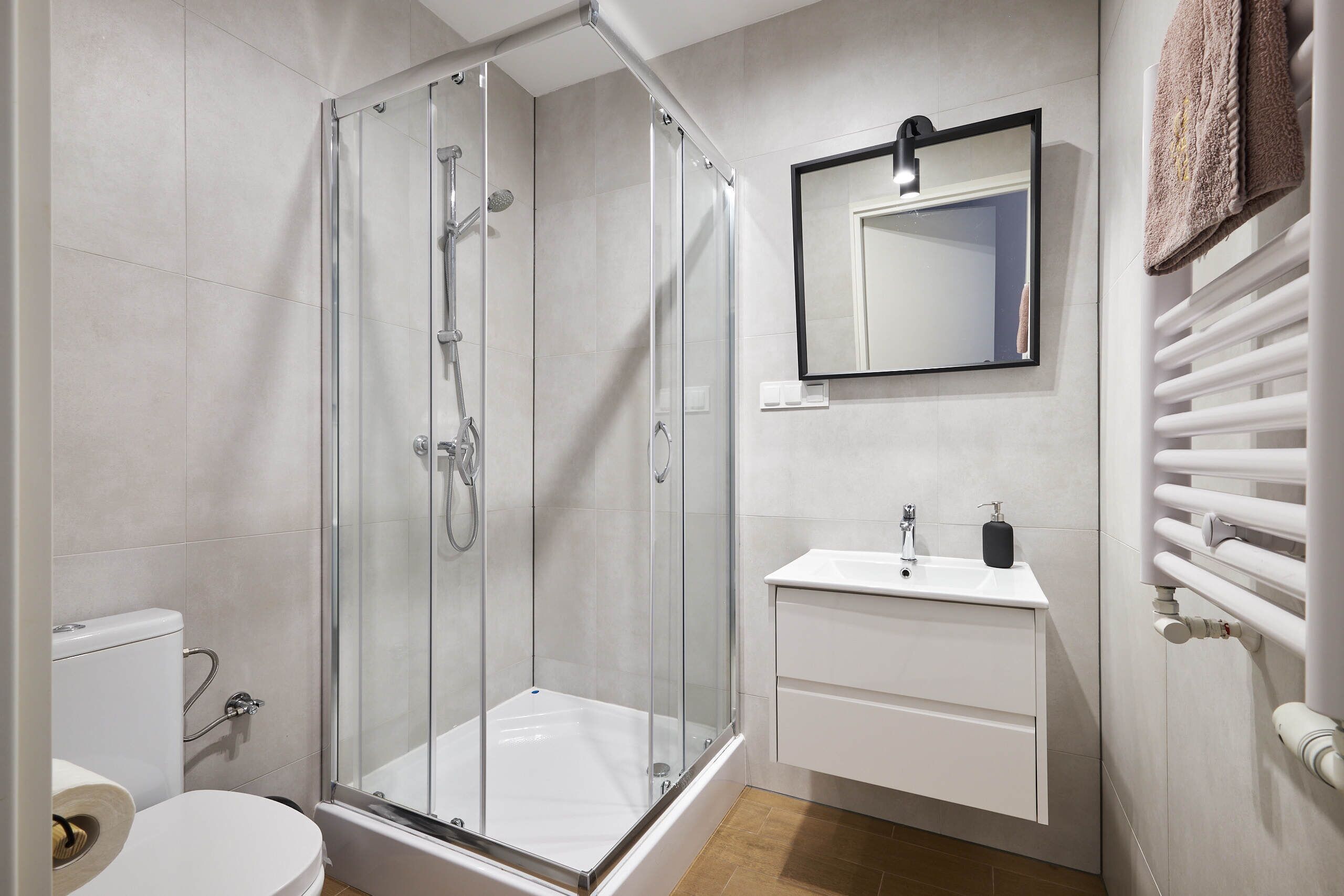 A modern bathroom with a glass-enclosed shower, a white sink, and a towel rack.