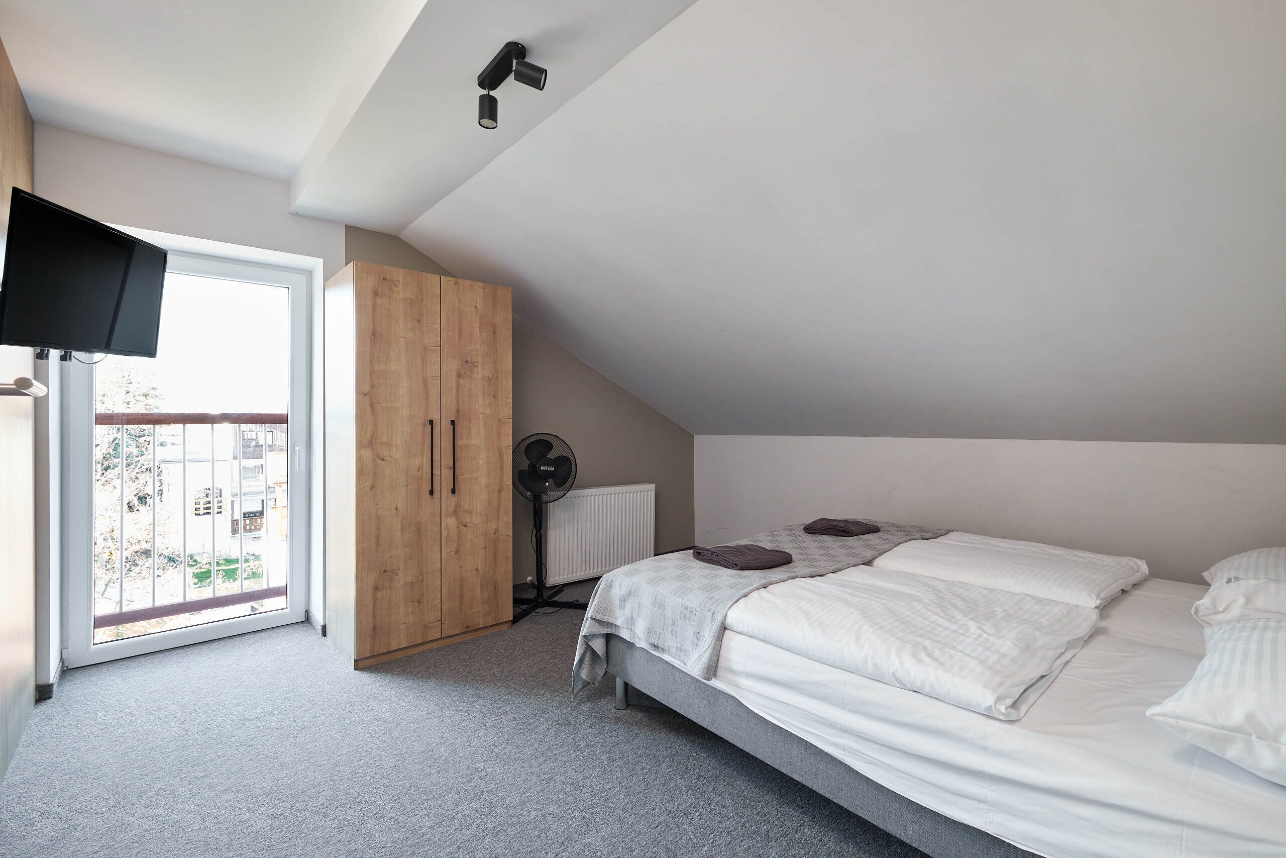 A bedroom with a bed, a wooden wardrobe, a radiator, and a window.