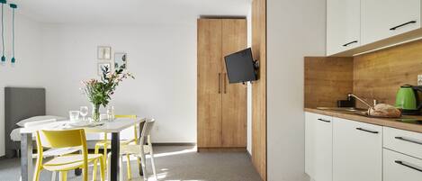A modern kitchen with white cabinets, a wooden door, and a flat-screen TV mounted on the wall.