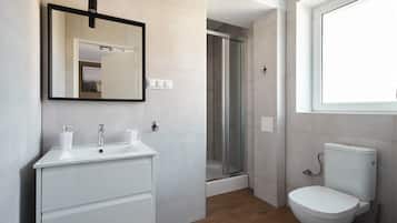 A modern bathroom with a white sink, mirror, and toilet, a shower area, and a window.