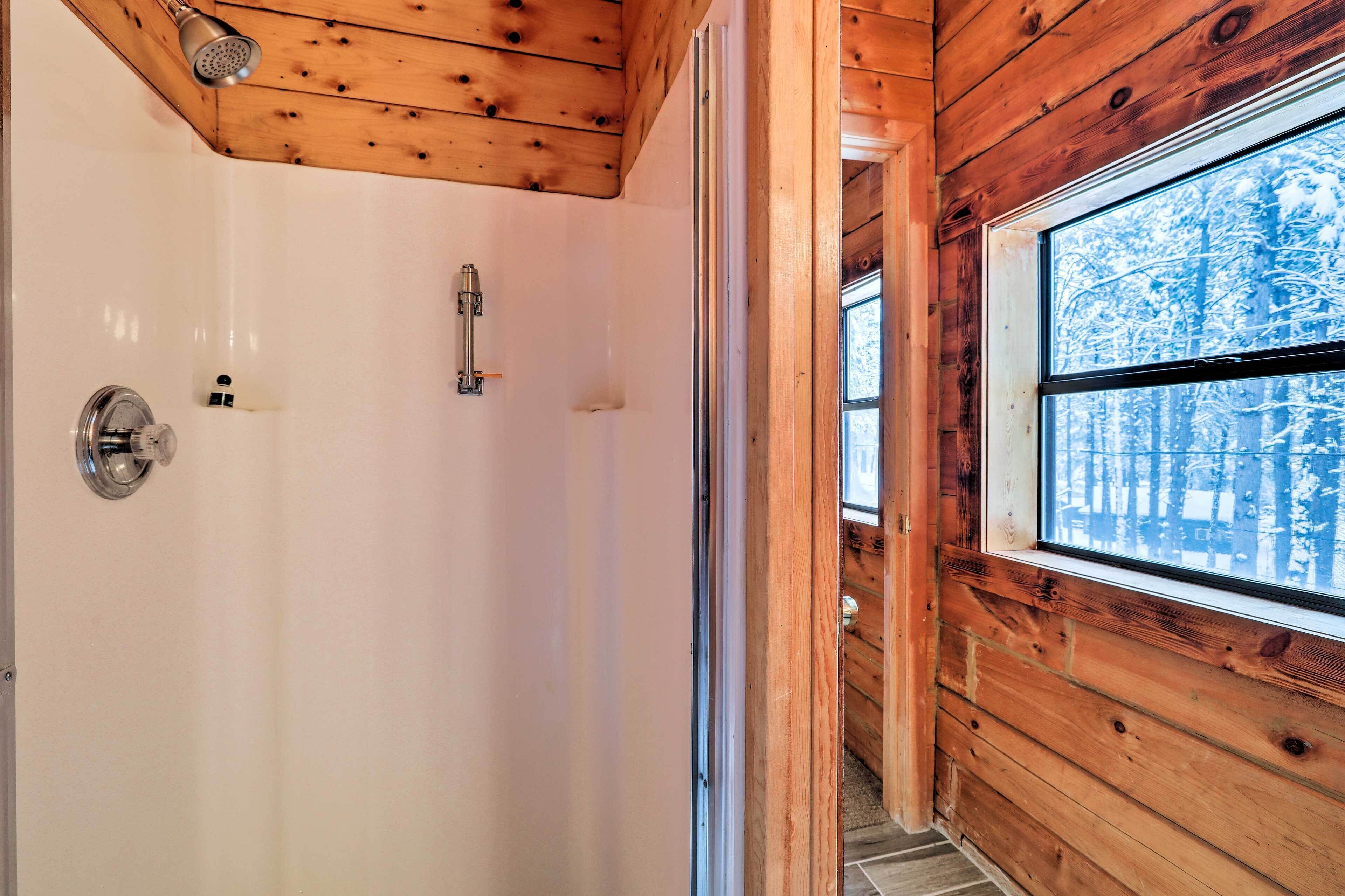 A wooden cabin interior with a shower, a window with a snowy forest view, and a door.