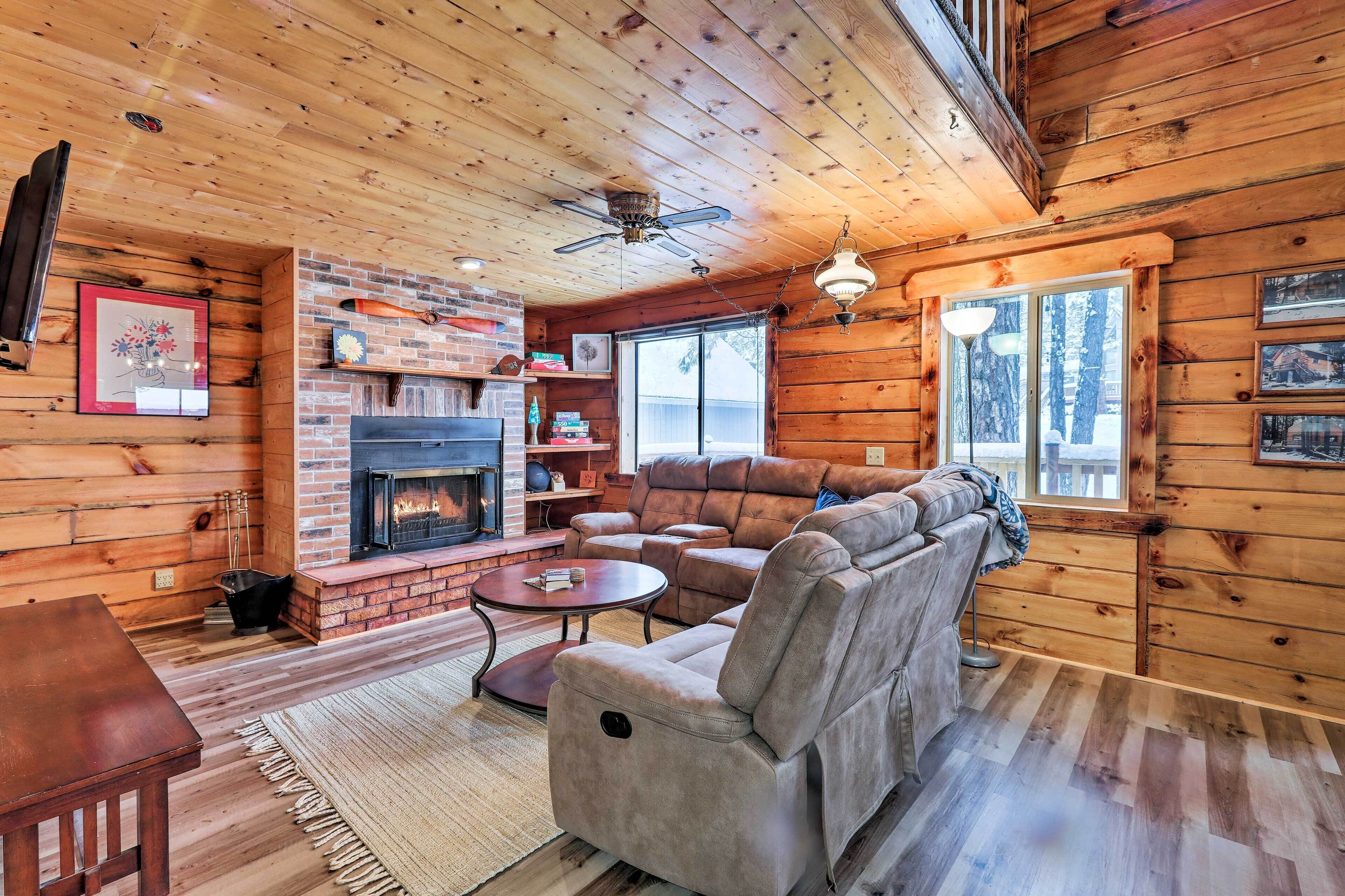 A cozy log cabin interior with a fireplace, leather sofa, and a ceiling fan.
