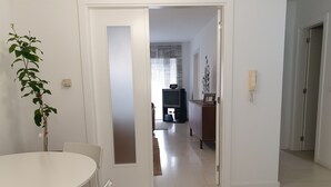 Ein Zimmer mit Esstisch und Stühlen, einer Pflanze und einem Fernseher im Hintergrund.