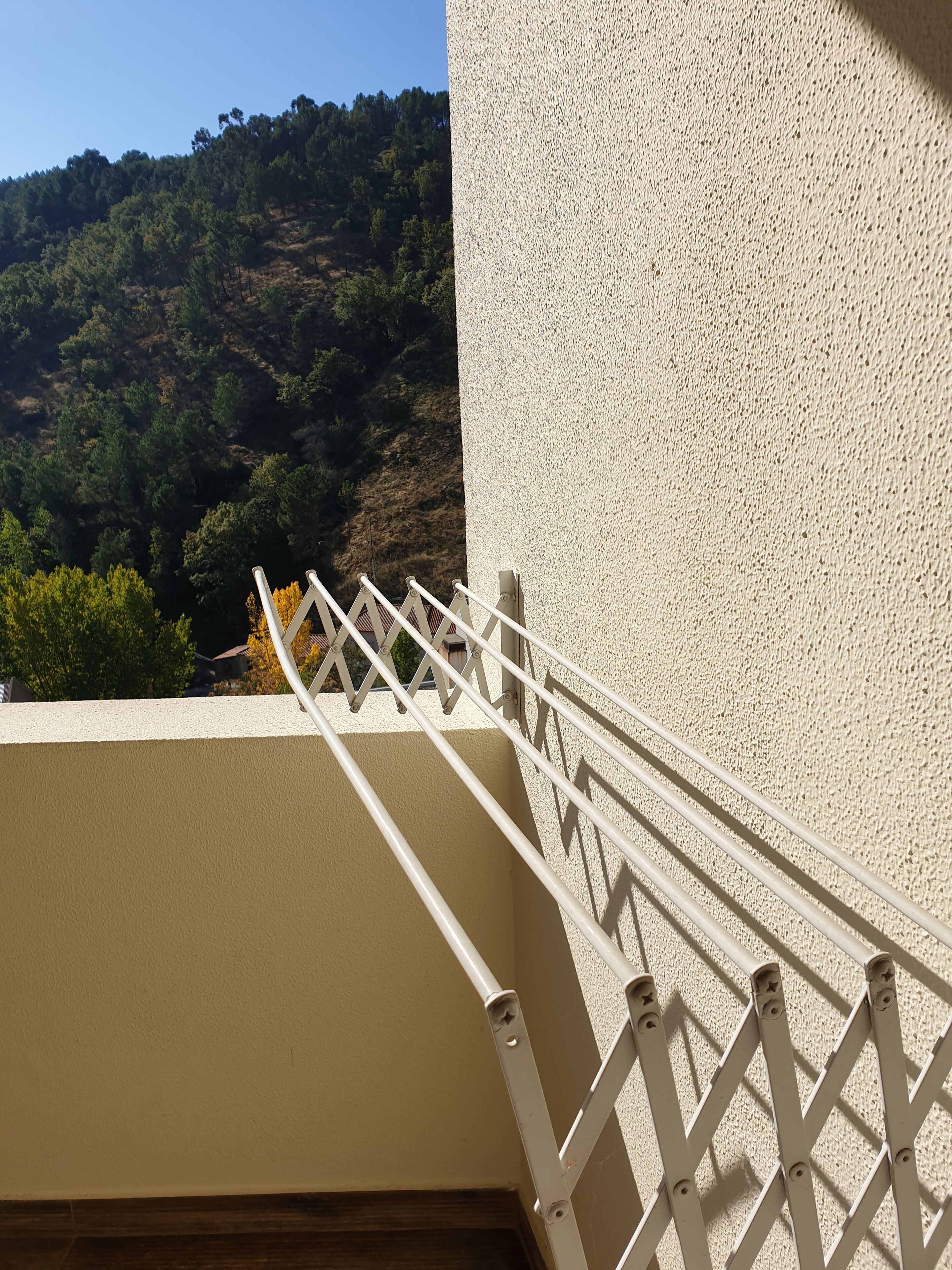 Un balcon doté d’une rambarde en métal, donnant sur une colline boisée.