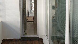Ein Flur mit Holzboden, einer Glastür zu einem Zimmer und einem großen Fenster mit Jalousien.