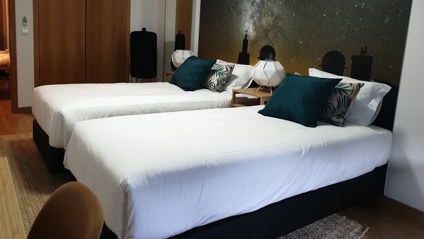 Ein Hotelzimmer mit zwei Betten, einem Nachttisch, einer Lampe und einem großen Wandbild der Milchstraße.