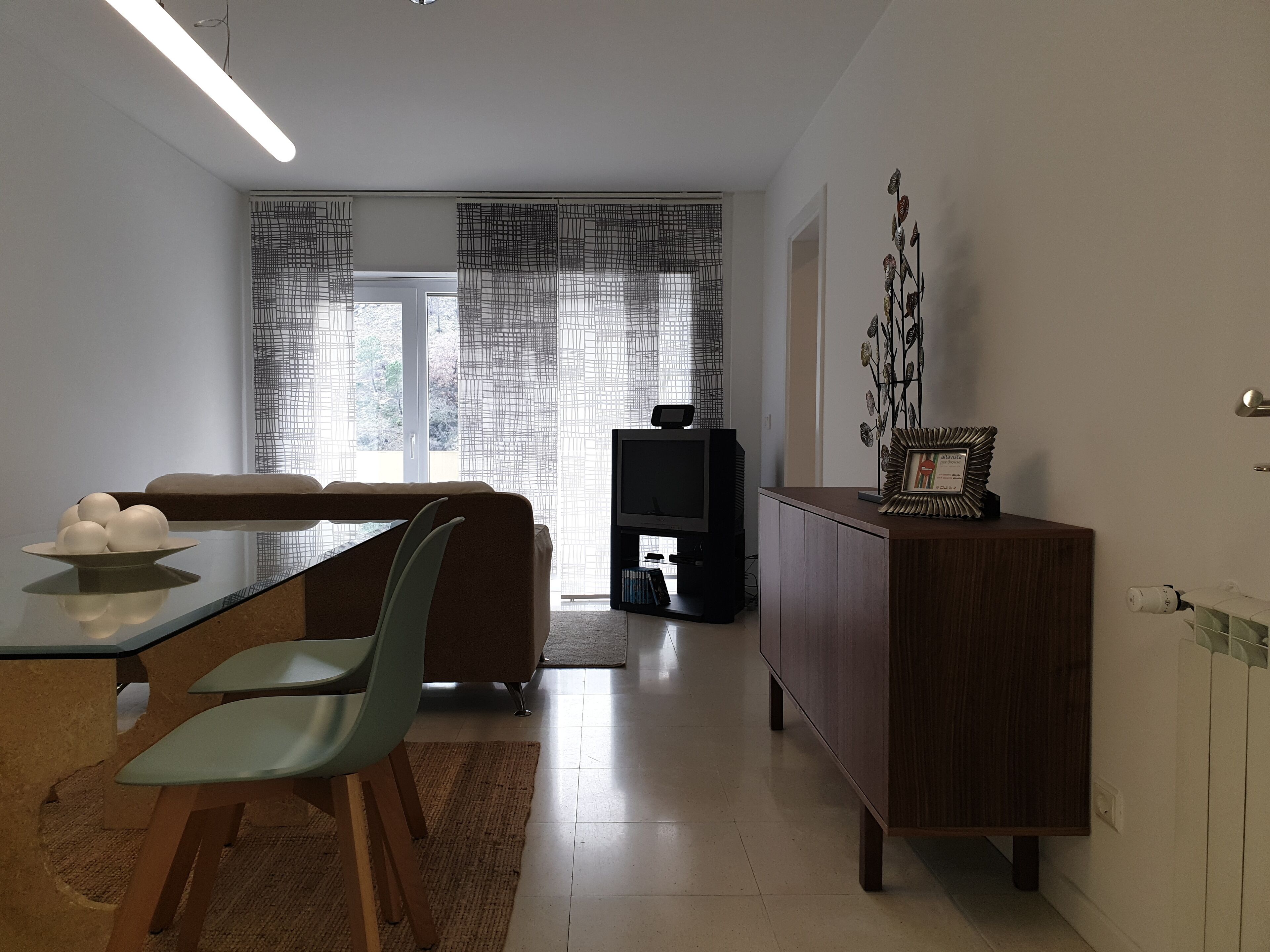 A modern living room with a dining area, a sofa, a TV, and a decorative plant.