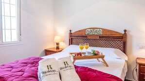 Ein ordentlich bezogenes Bett mit einer rosafarbenen Tagesdecke, zwei mit einem Logo versehene Kissen, ein Tablett mit Frühstücksartikeln und ein Holz-Kopfteil.