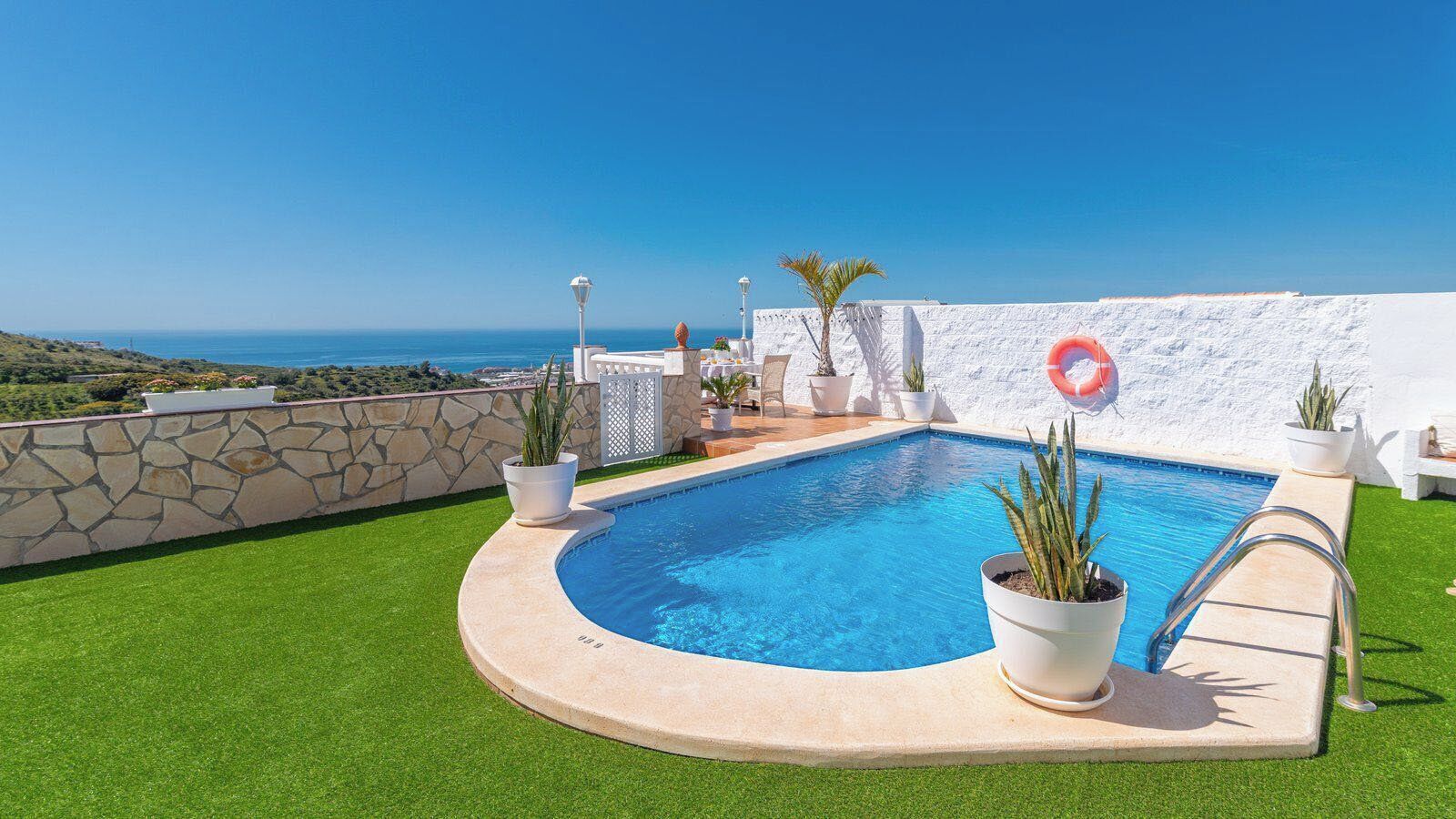 A pool with a clear view of the sea, surrounded by a stone wall and potted plants.