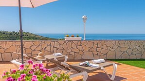 Una terraza con muros de piedra, vistas al mar y sillones con toallas.